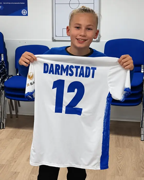 Noah hält sein Trikot des SV Darmstadt 98 mit der Nummer 12 in die Kamera